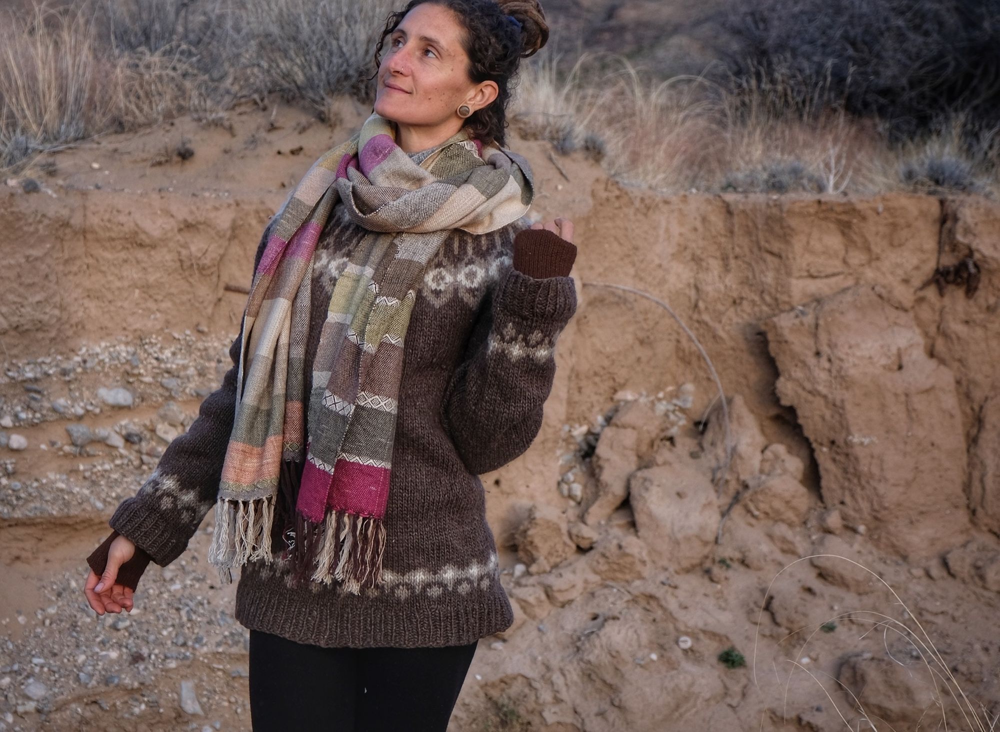 A woman wearing a handwoven silk fabric in soft rainbow striped shades, naturally dyed, in a desert landscape