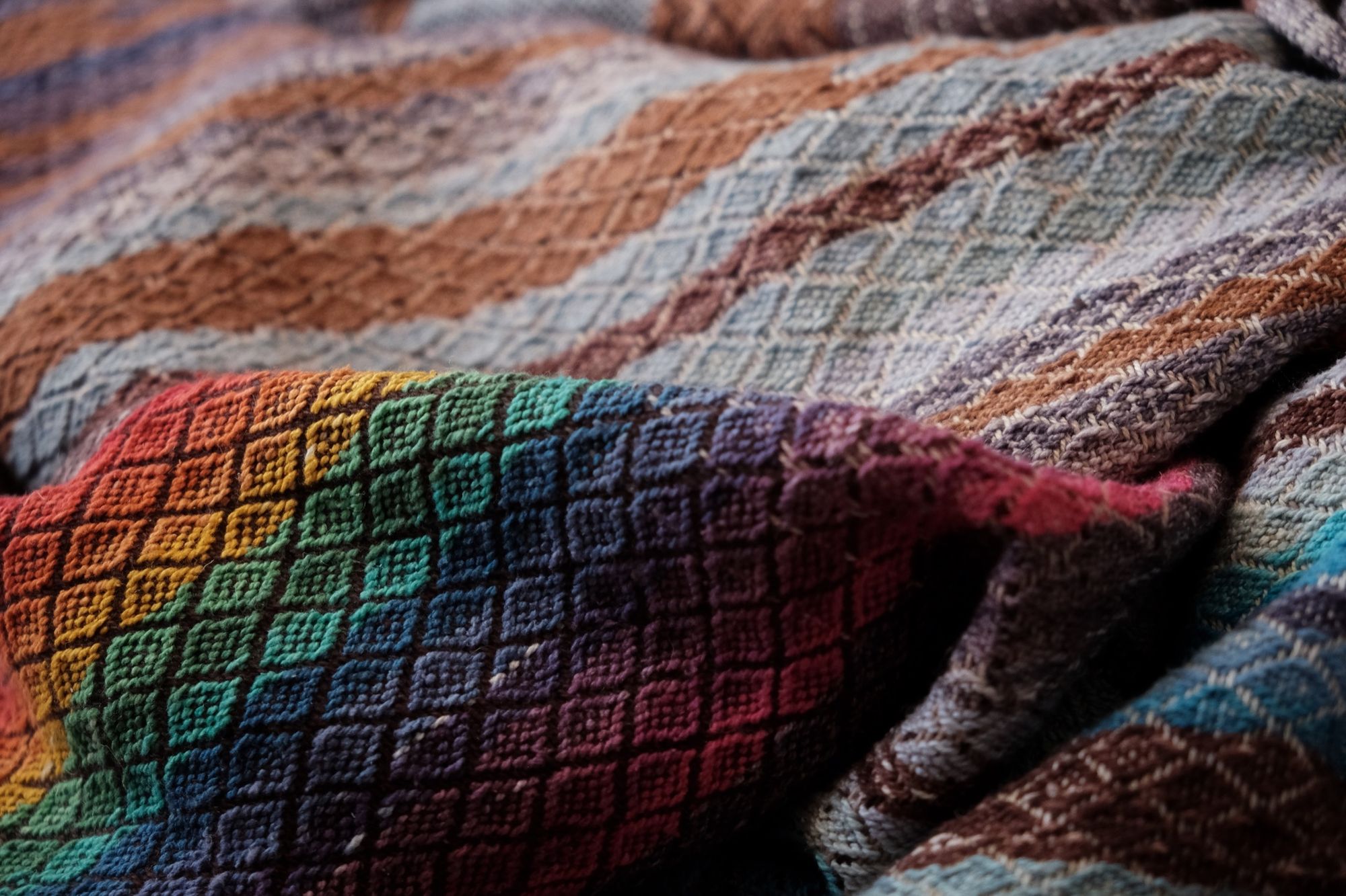 Handwoven fabric with a diamond weave pattern in shades of brown, blue and rainbow lays on a wooden floor