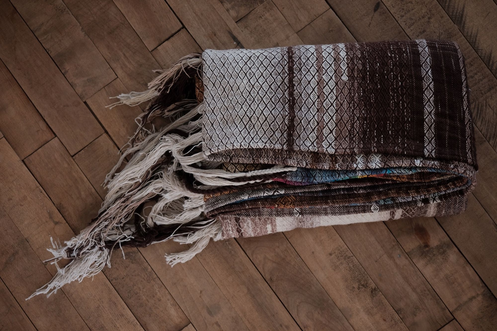Handwoven fabric with a diamond pattern in brown, cream, white and rainbow colors, folded on a wood floor