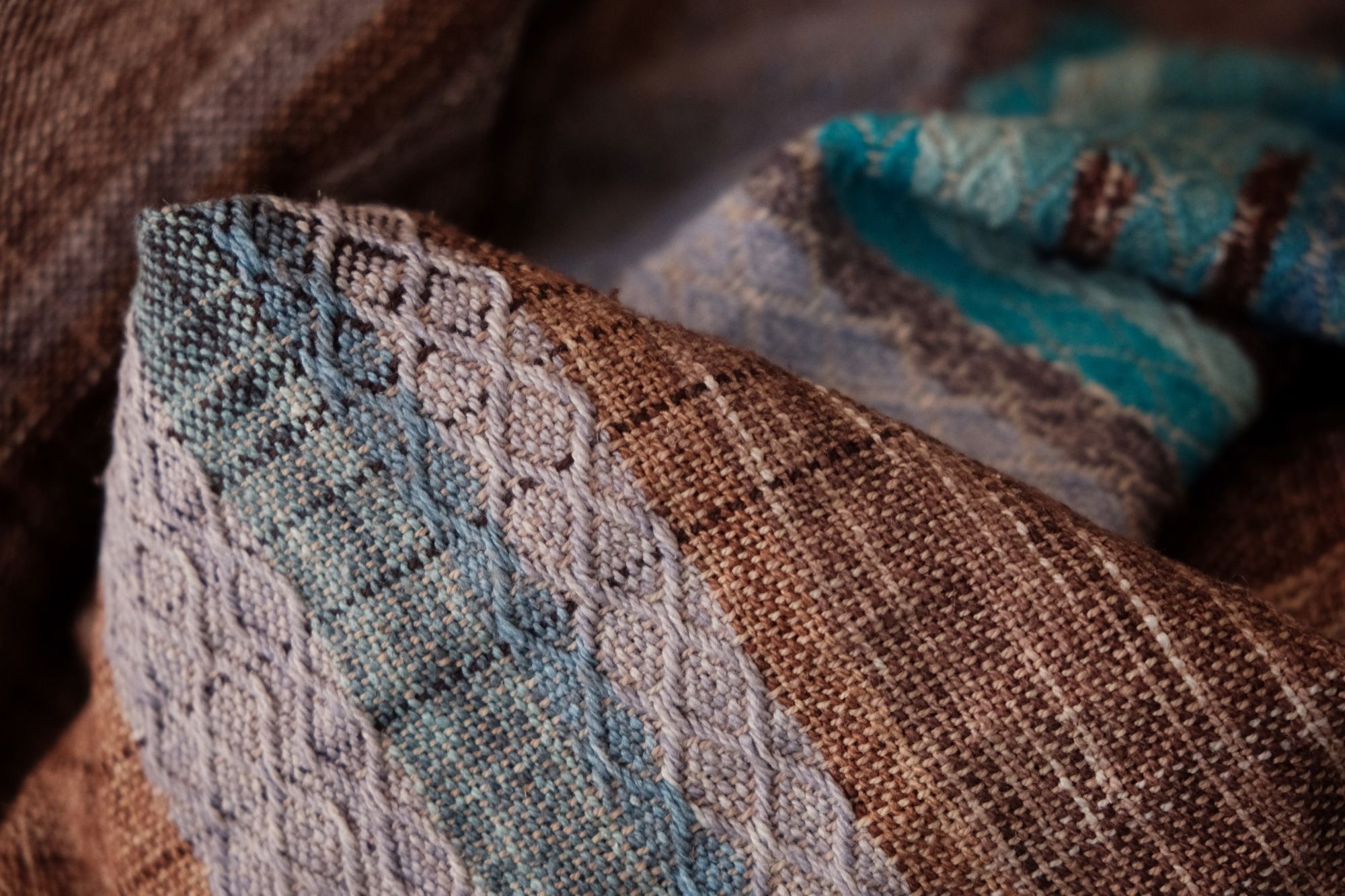 Handwoven fabric with a diamond weave pattern in shades of brown, blue and rainbow lays on a wooden floor