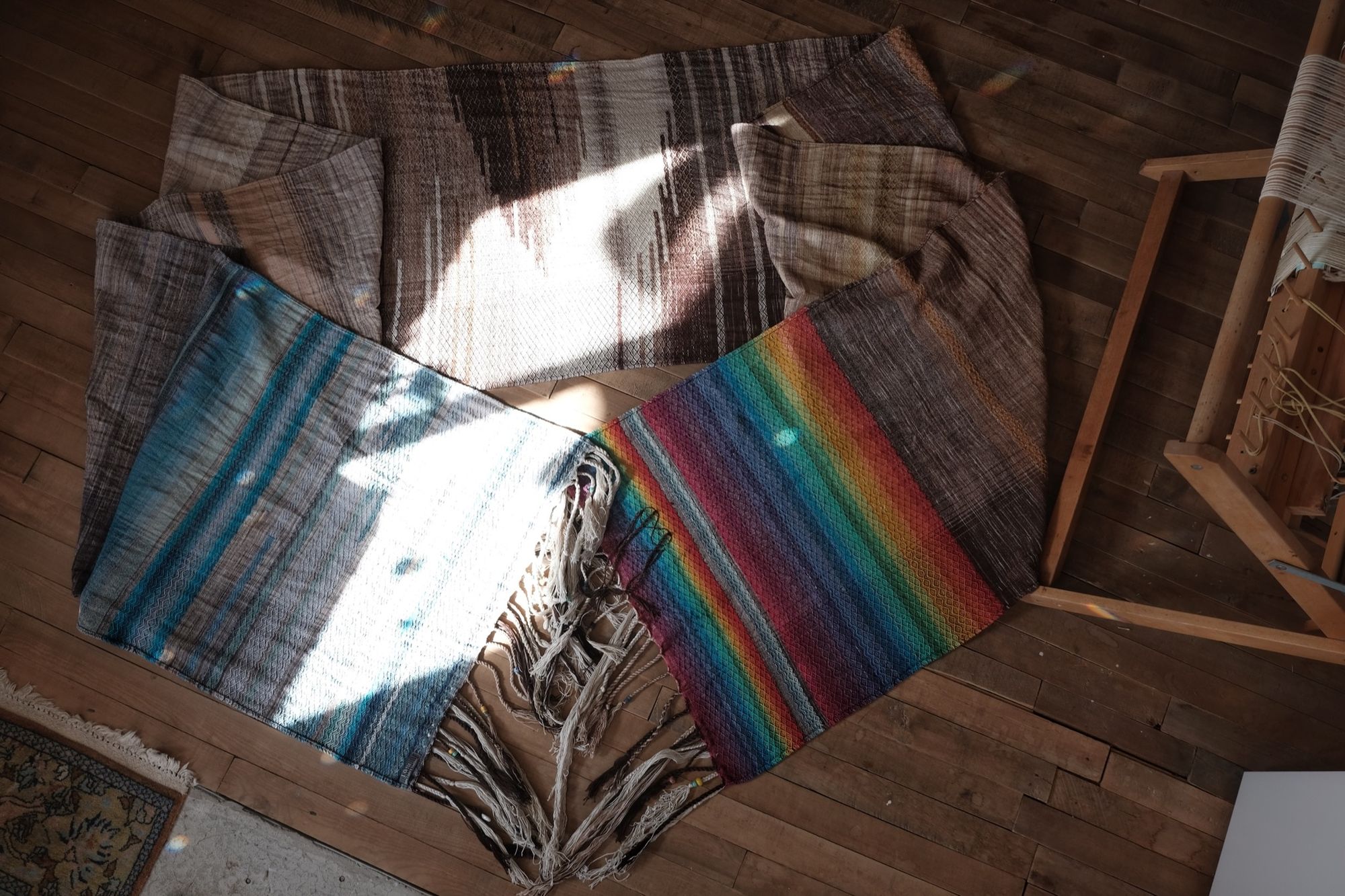 Handwoven fabric with a diamond pattern in brown, cream, white and rainbow colors laying on a wooden floor