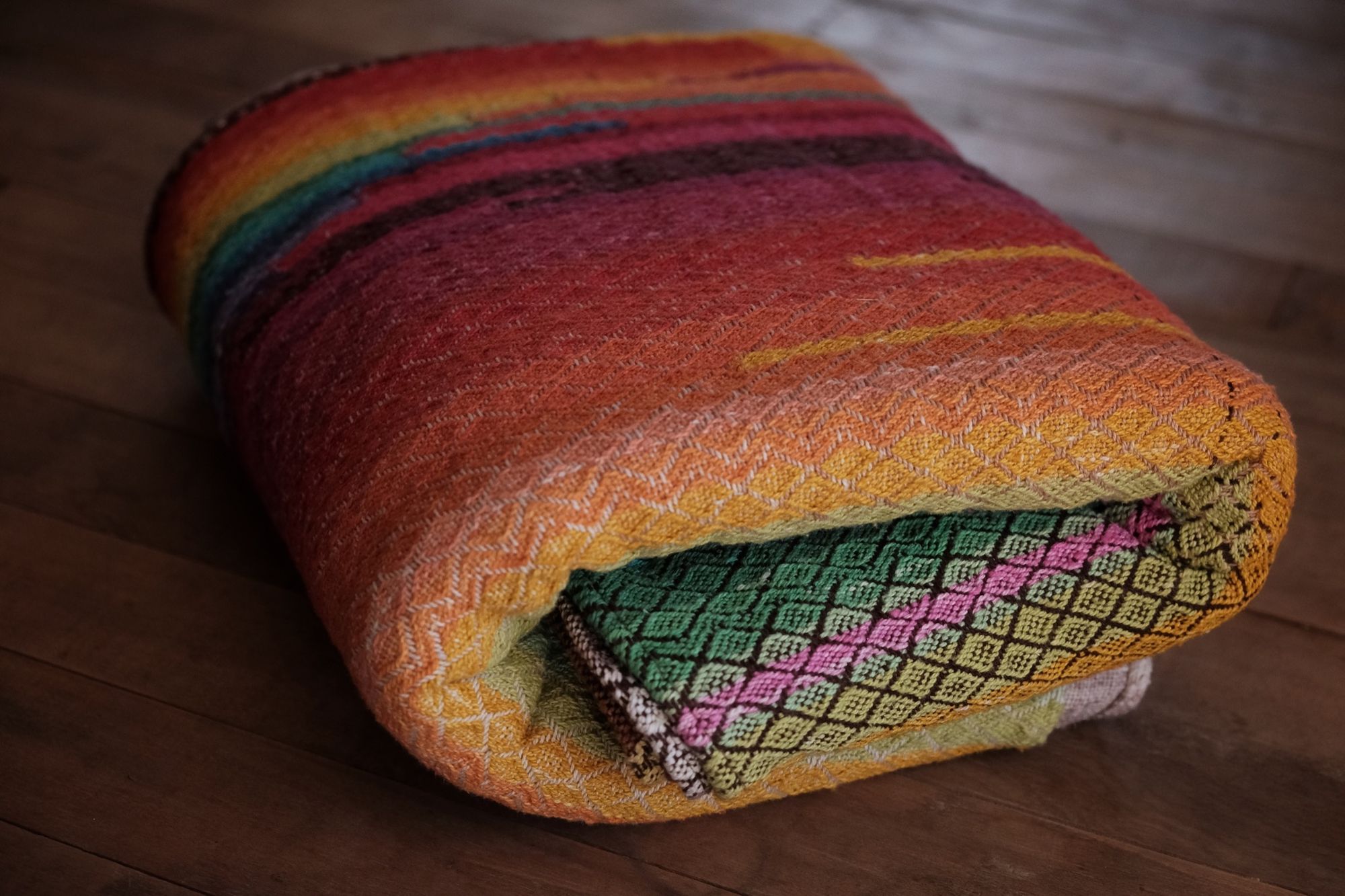 handwoven raw silk fabric woven with a diamond pattern in rainbow, gray, brown and cream colors folded on a wooden floor