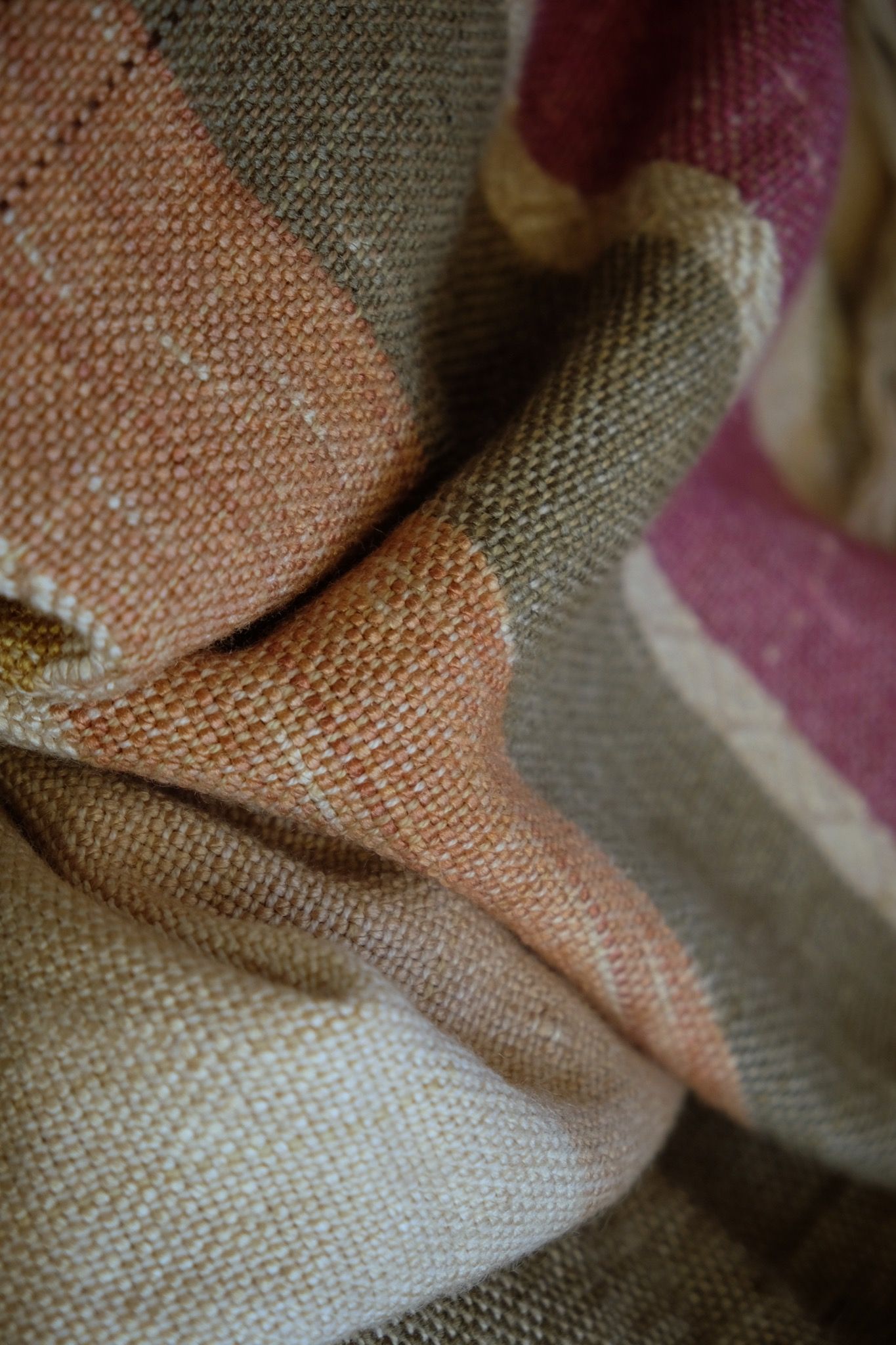 A detail of handwoven silk fabric in soft rainbow striped shades, naturally dyed, laying folded on the floor