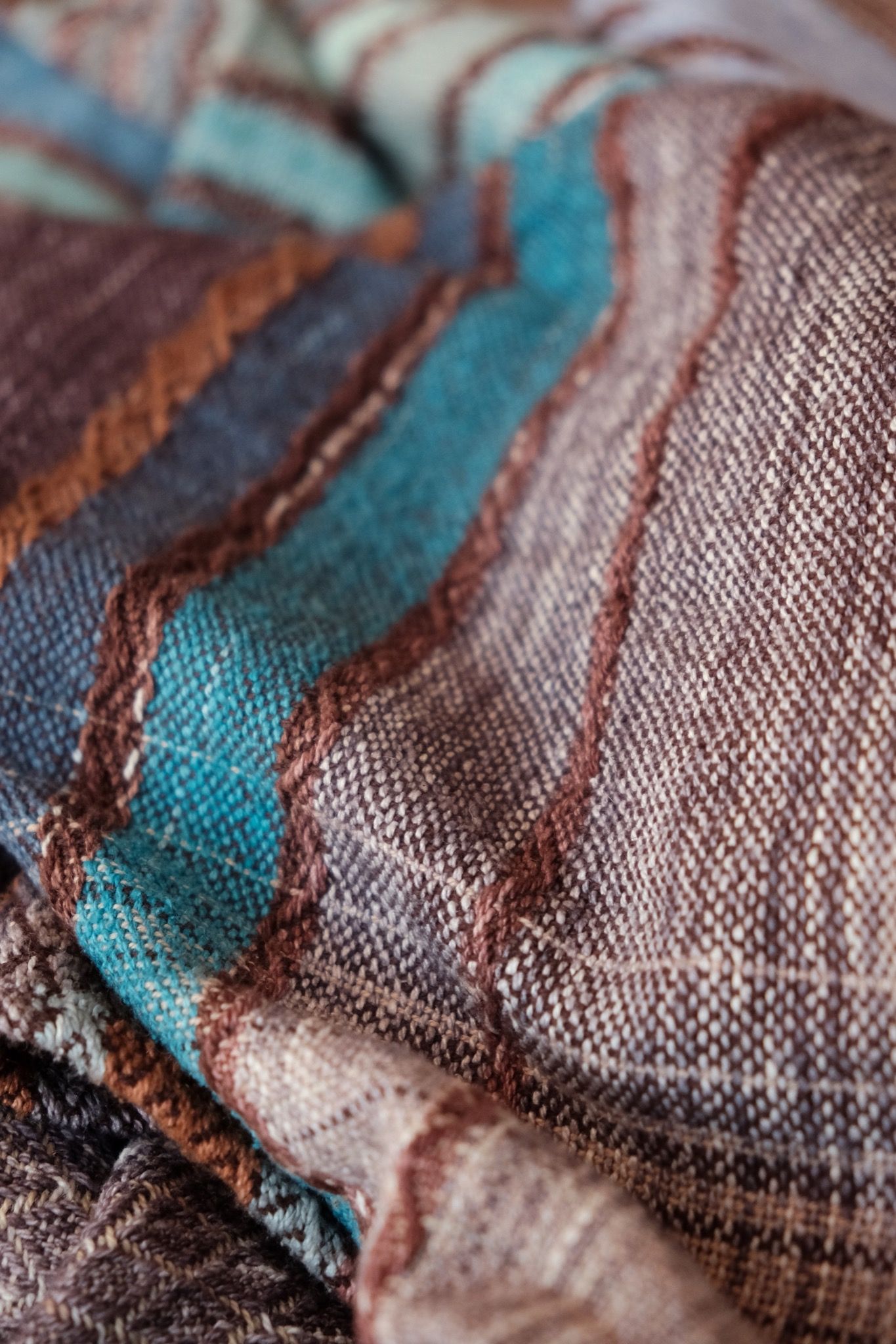 Handwoven fabric with a diamond weave pattern in shades of brown, blue and rainbow lays on a wooden floor