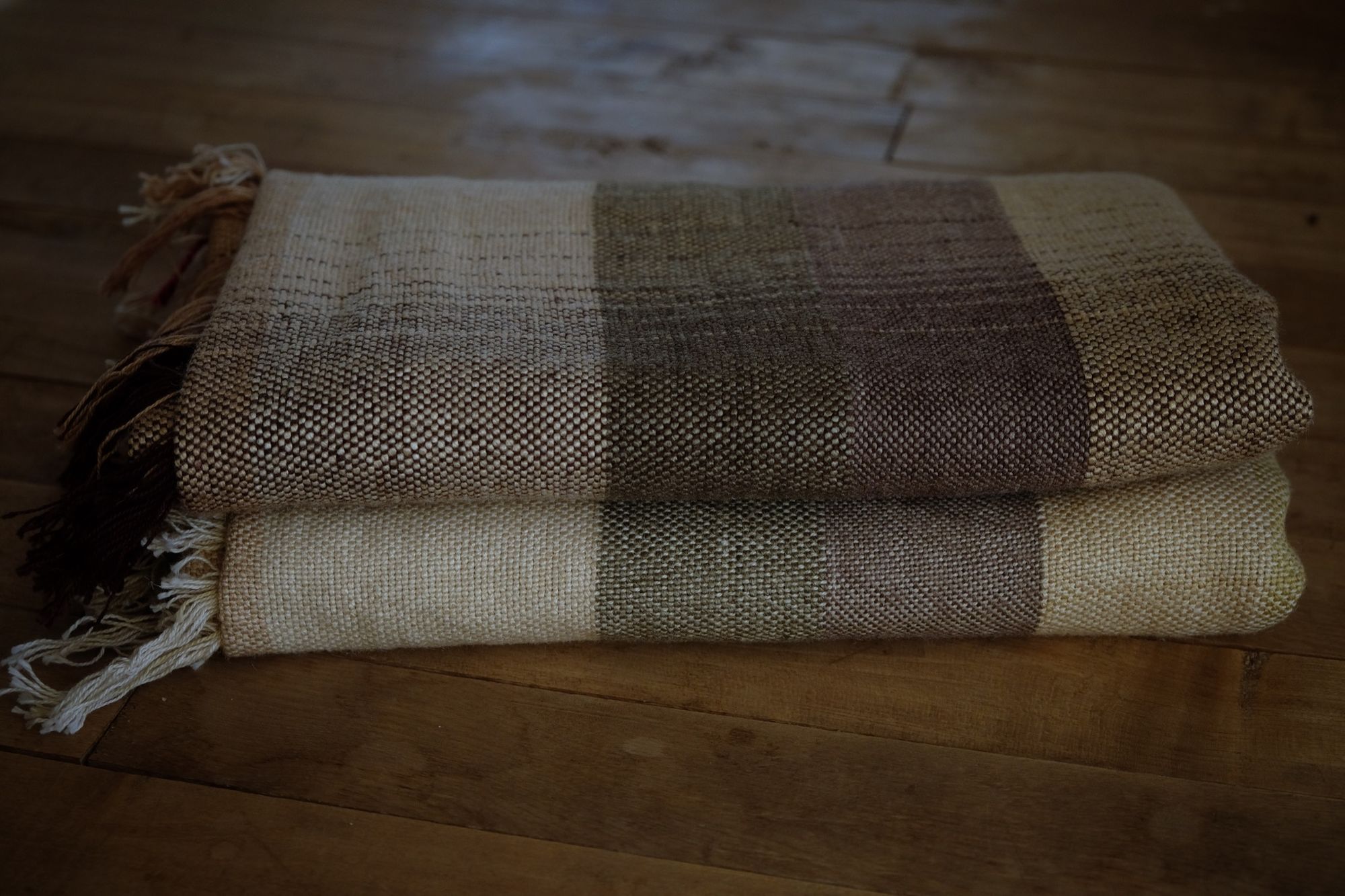 A detail of handwoven silk fabric in soft rainbow striped shades, naturally dyed, laying folded on the floor