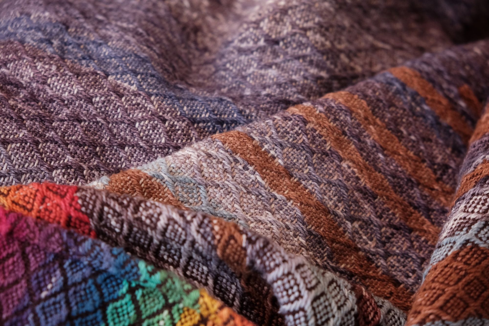 Handwoven fabric with a diamond weave pattern in shades of brown, blue and rainbow lays on a wooden floor