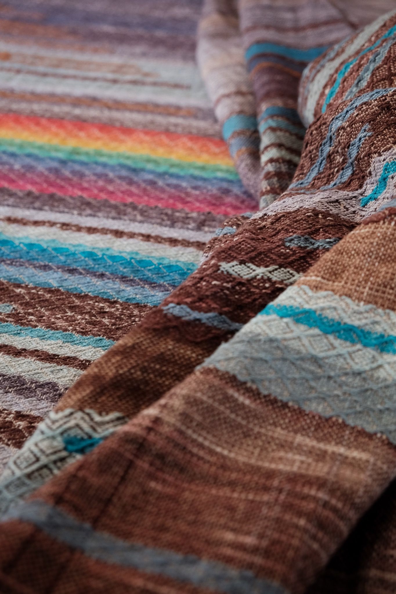 Handwoven fabric with a diamond weave pattern in shades of brown, blue and rainbow lays on a wooden floor