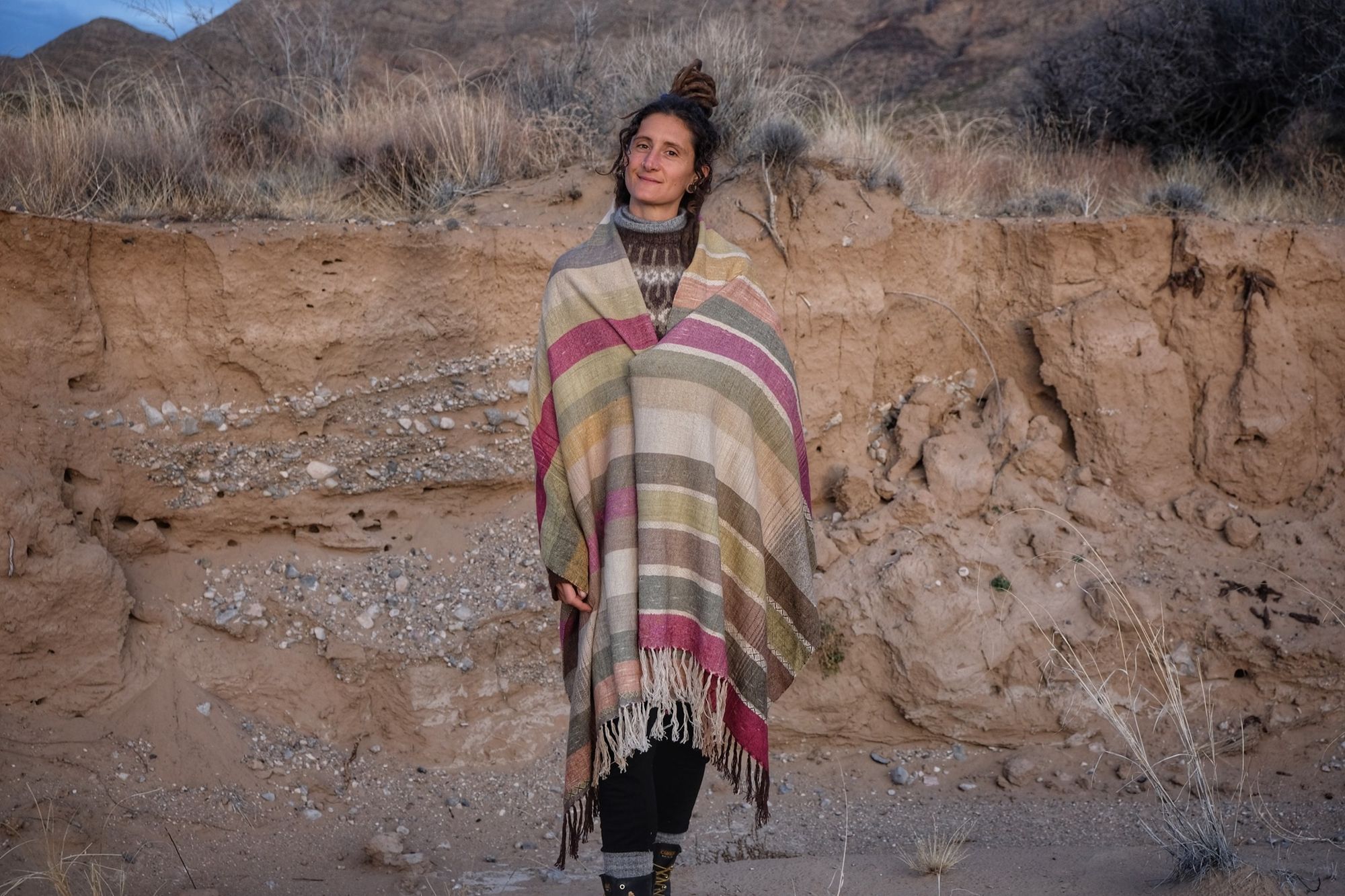 A woman wearing a handwoven silk fabric in soft rainbow striped shades, naturally dyed, in a desert landscape