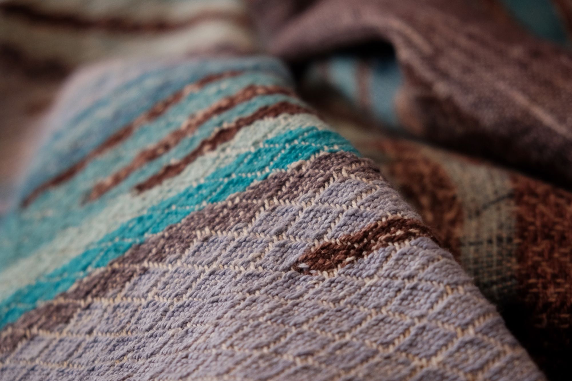 Handwoven fabric with a diamond weave pattern in shades of brown, blue and rainbow lays on a wooden floor