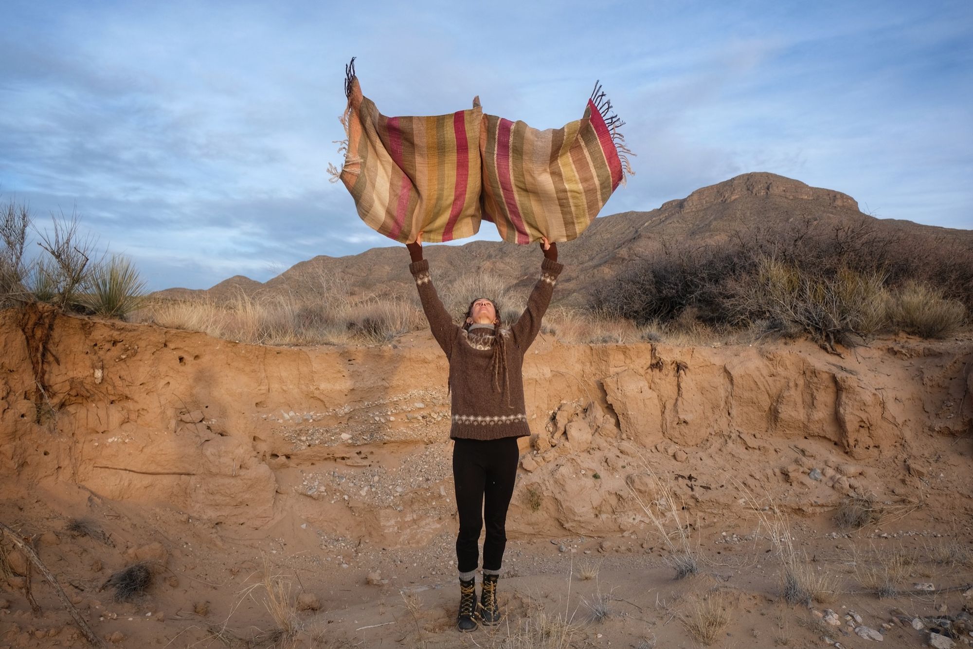 A woman wearing a handwoven silk fabric in soft rainbow striped shades, naturally dyed, in a desert landscape