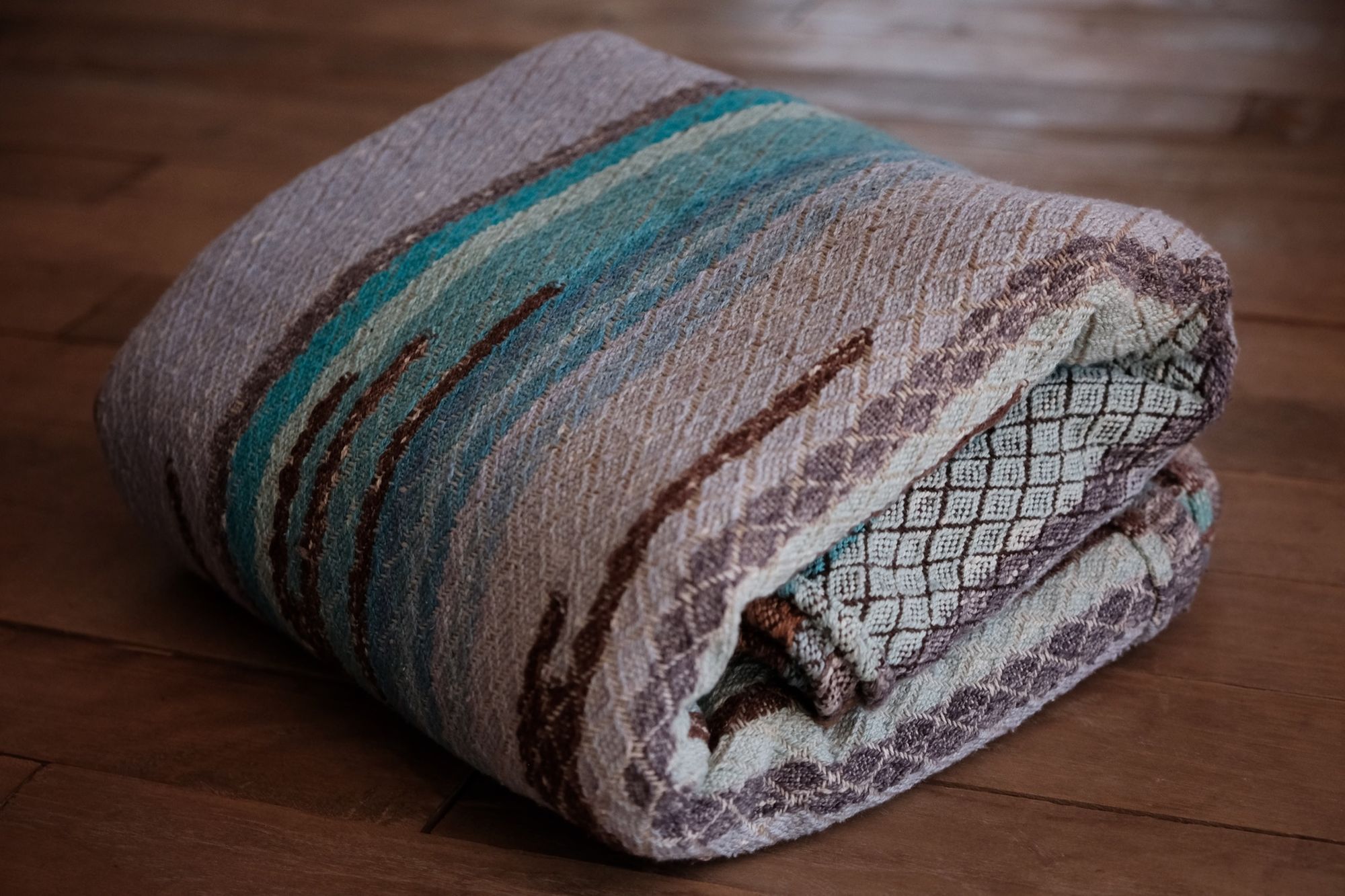 Handwoven fabric with a diamond weave pattern in shades of brown, blue and rainbow lays on a wooden floor