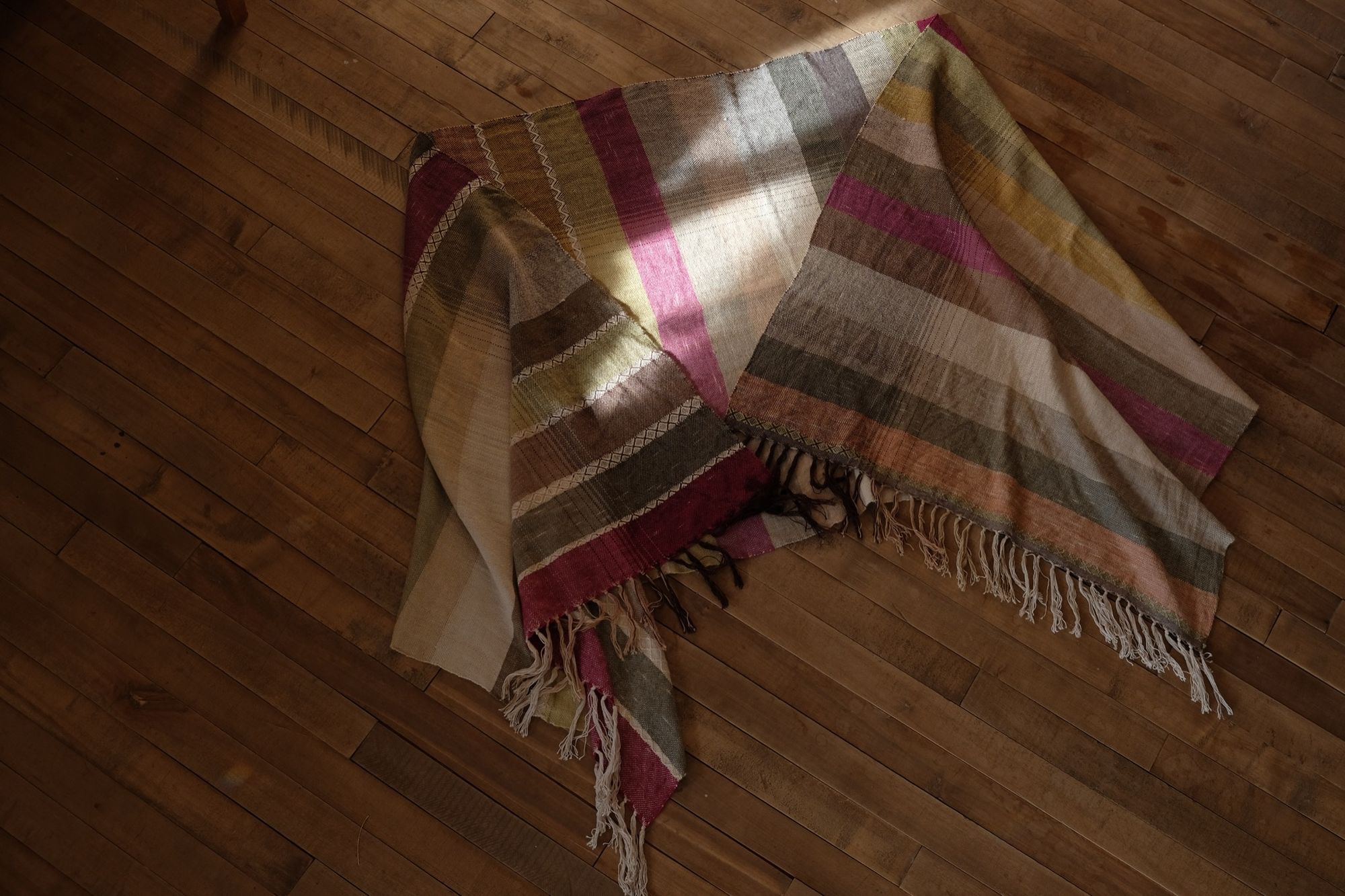 A detail of handwoven silk fabric in soft rainbow striped shades, naturally dyed, laying on a wooden floor