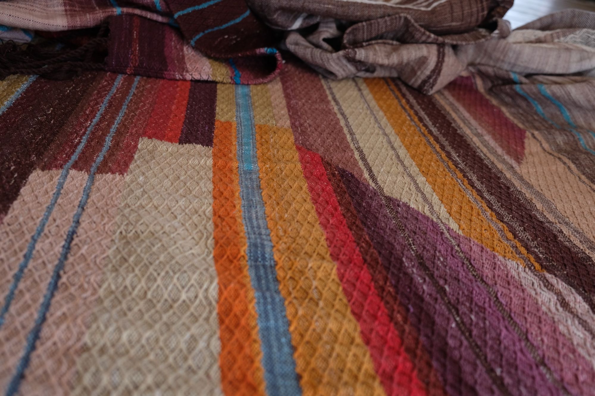 Detail of Handwoven fabric with a diamond texture pattern in natural browns, grey, purples, reds, turquoise, yellow, orange and pink.