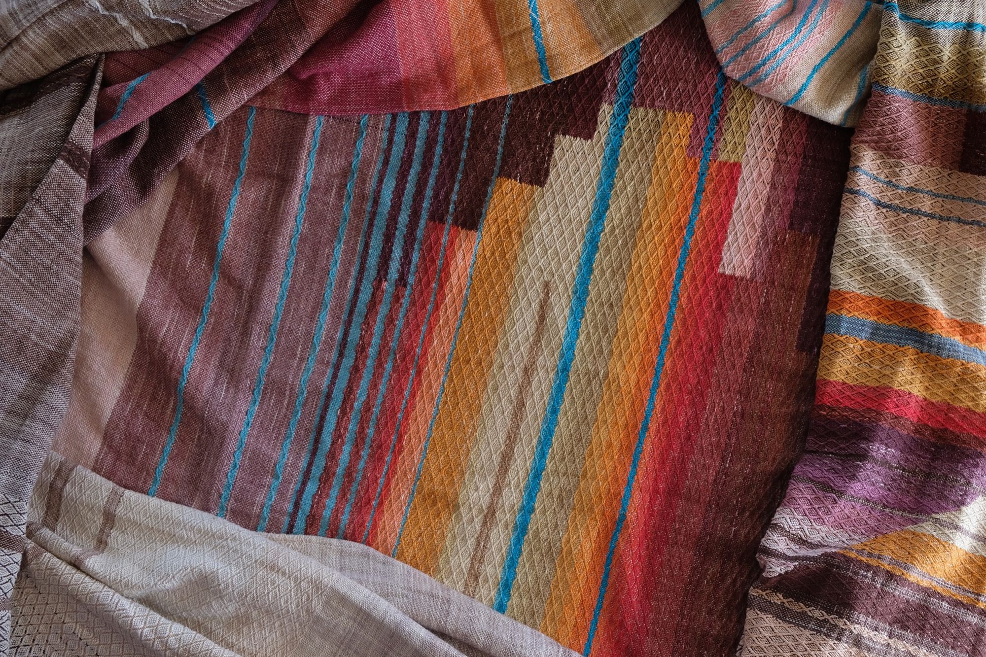Detail of Handwoven fabric with a diamond texture pattern in natural browns, grey, purples, reds, turquoise, yellow, orange and pink.