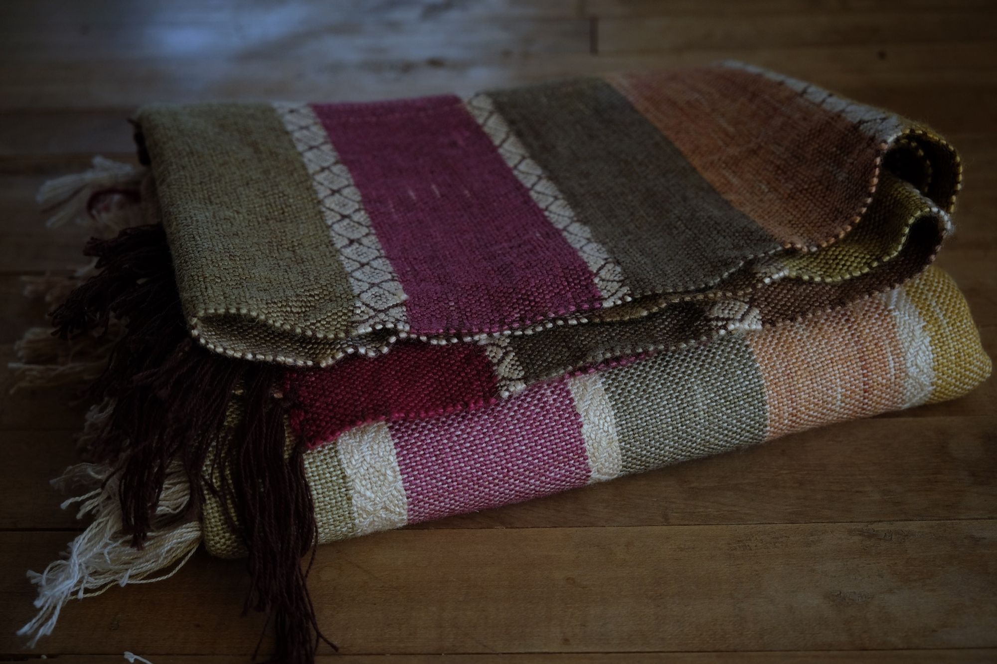 A detail of handwoven silk fabric in soft rainbow striped shades, naturally dyed, laying folded on the floor