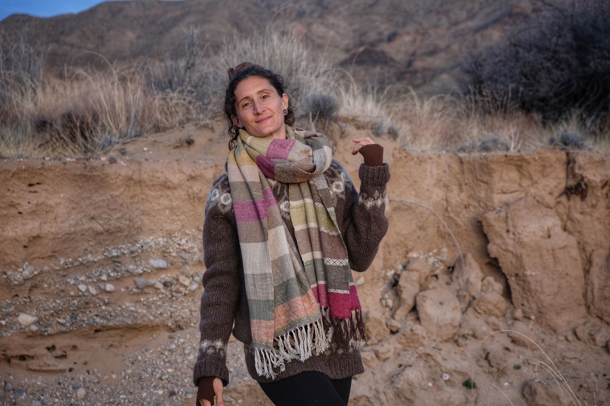 A woman wearing a handwoven silk fabric in soft rainbow striped shades, naturally dyed, in a desert landscape