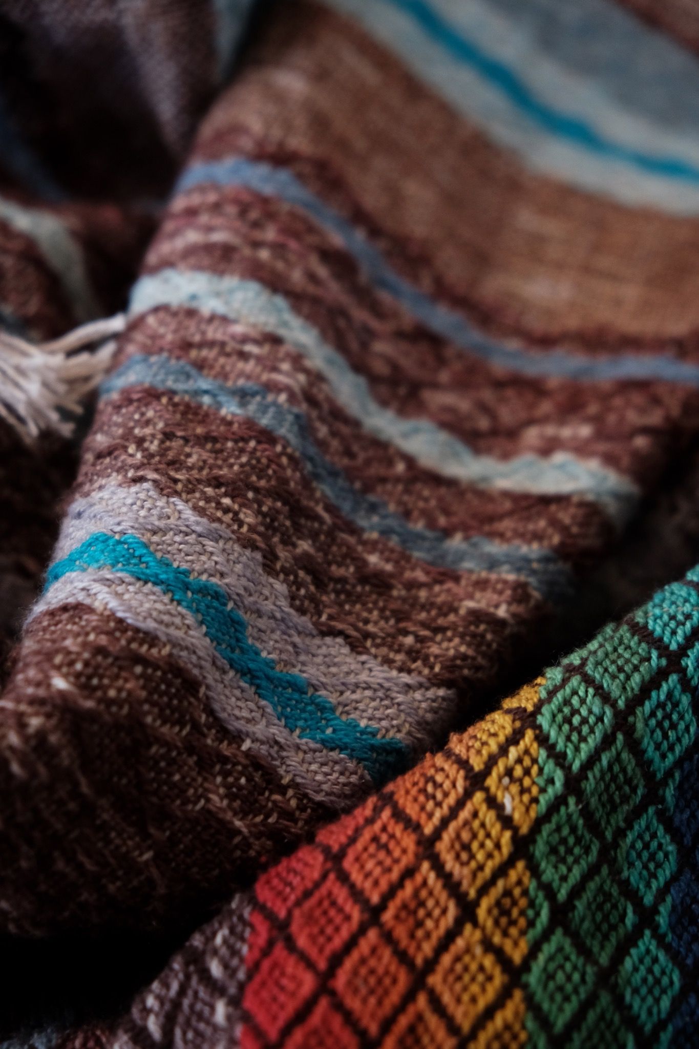 Handwoven fabric with a diamond weave pattern in shades of brown, blue and rainbow lays on a wooden floor