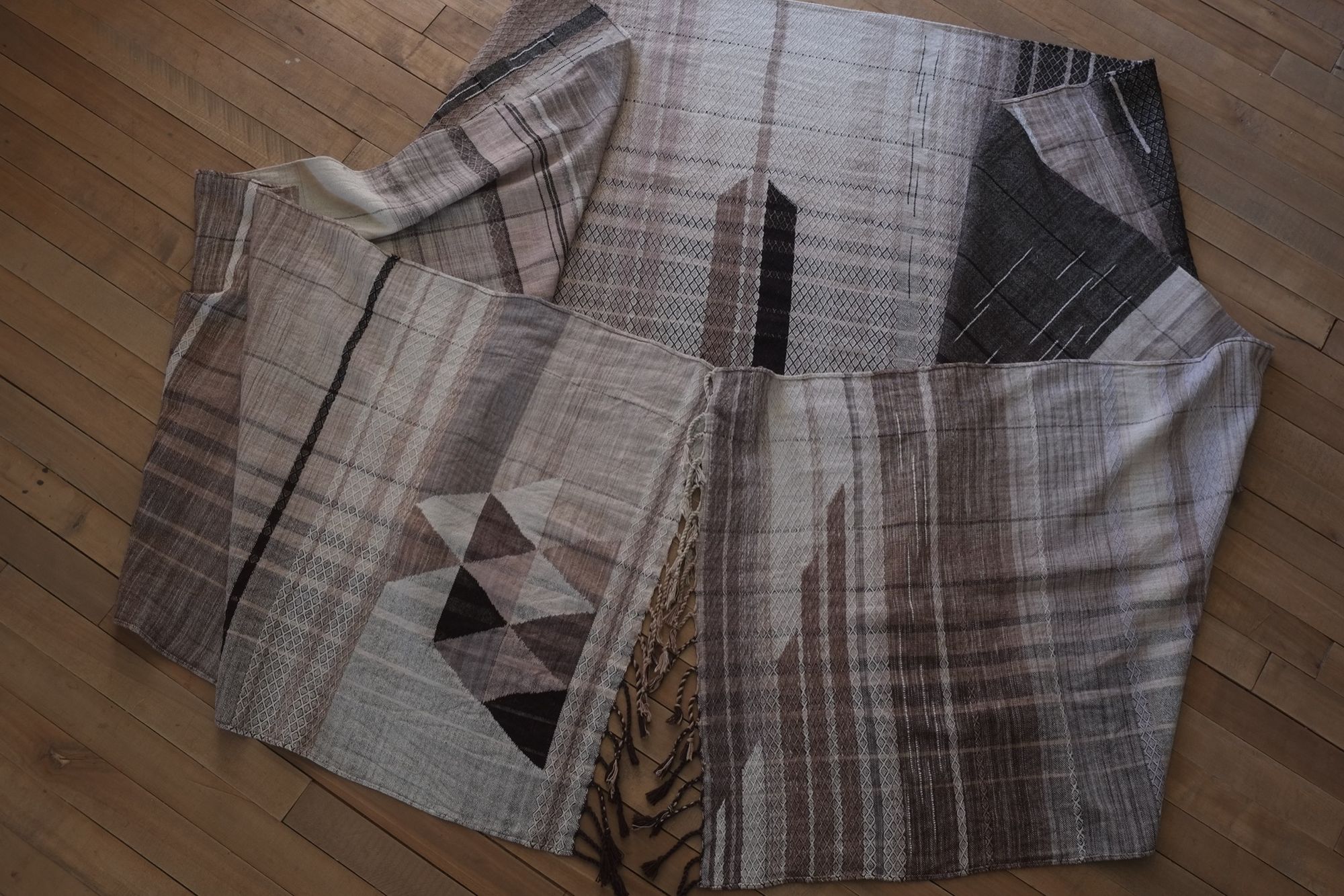 Detail of handwoven highly textured diamond pattern raw silk fabric in monochrome colors laying on a wooden floor