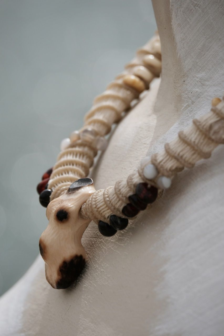 A white mannequin wears a white sculptural tubular knot work necklace with beads and a walrus tooth goddess at the center