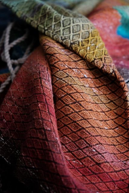 Detail of A handwoven diamond pattern rainbow shawl that rests on a wood floor 