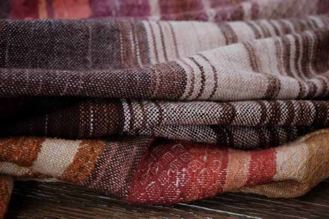 handwoven diamond pattern fabric in shades of red, pink, rust and purple lays on a wooden floor