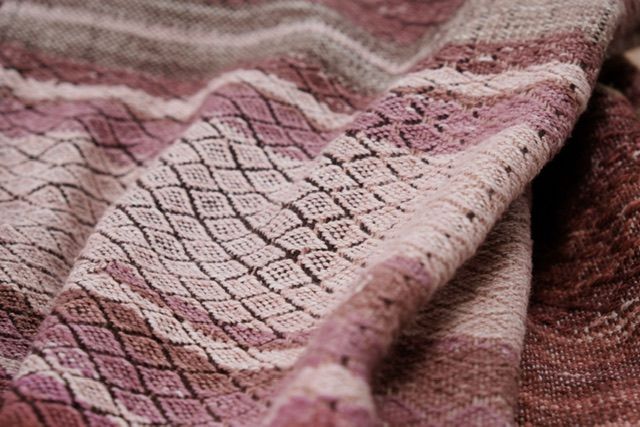 handwoven diamond pattern fabric in shades of red, pink, rust and purple lays on a wooden floor