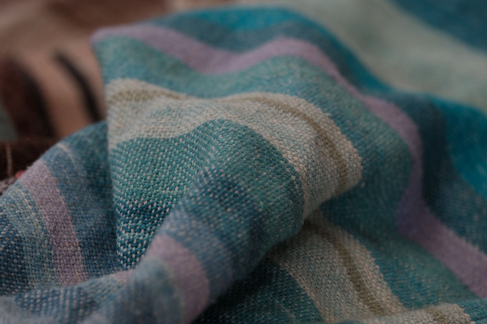 A detail of raw silk handwoven fabric in a rainbow of hand dyed colors with circular moon-like details 