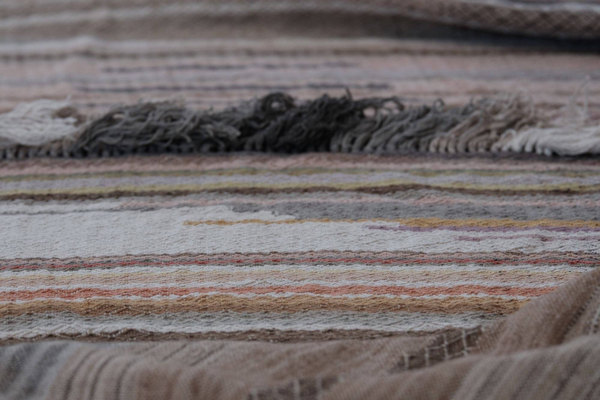 handwoven fabric of Naturally dyed subtle rainbow hues with a diamond texture pattern lays on a wooden floor