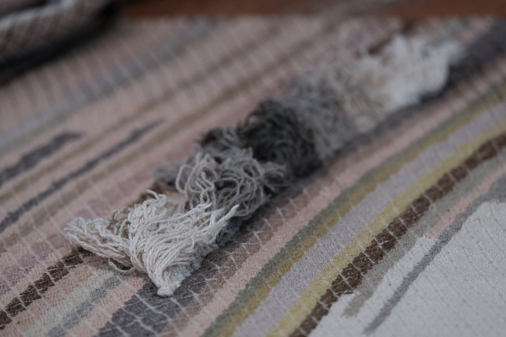 handwoven fabric of Naturally dyed subtle rainbow hues with a diamond texture pattern and graded gray fringe lays on a wooden floor