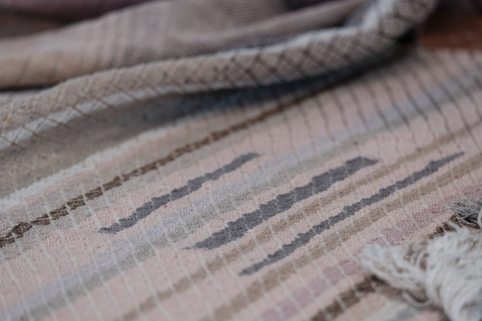 handwoven fabric of Naturally dyed subtle rainbow hues with a diamond texture pattern lays on a wooden floor