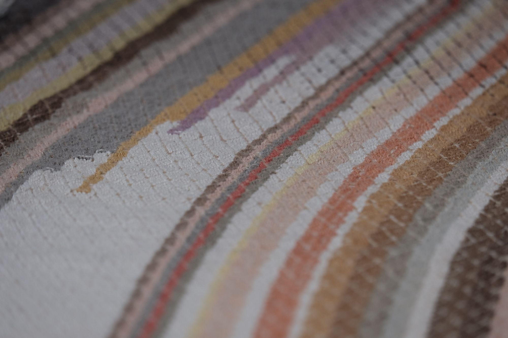 handwoven fabric of Naturally dyed subtle rainbow hues with a diamond texture pattern lays on a wooden floor