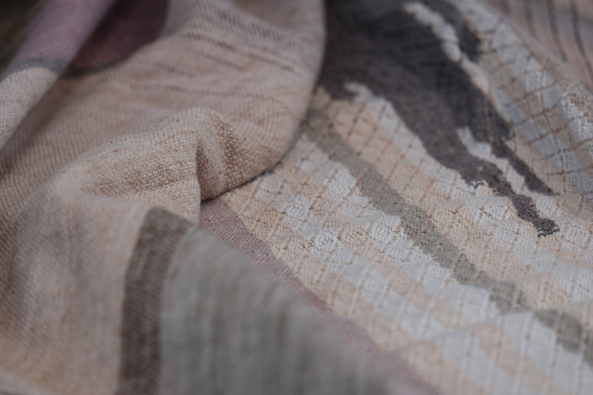 handwoven fabric of Naturally dyed subtle rainbow hues with a diamond texture pattern lays on a wooden floor