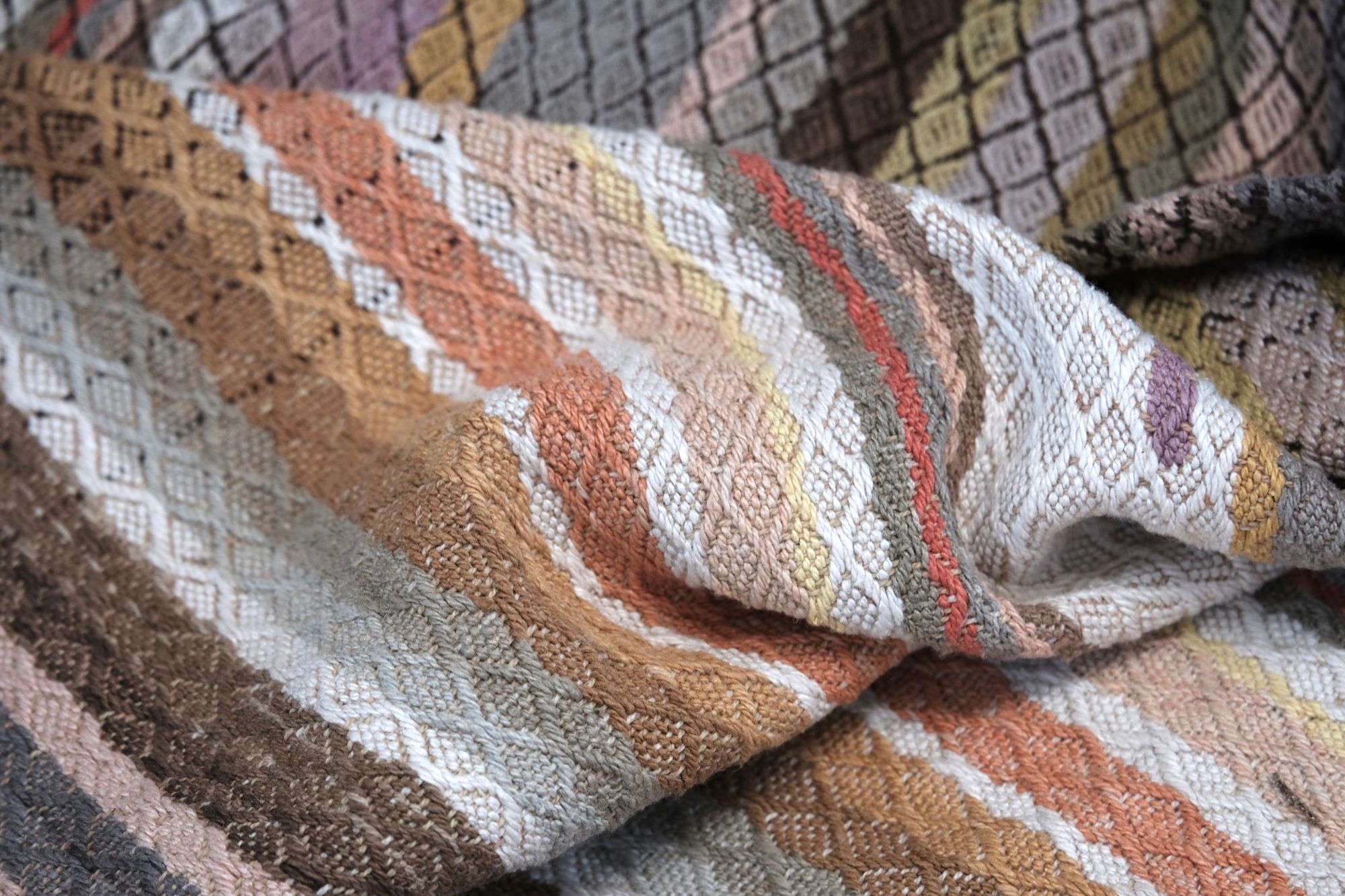 handwoven fabric of Naturally dyed subtle rainbow hues with a diamond texture pattern lays on a wooden floor