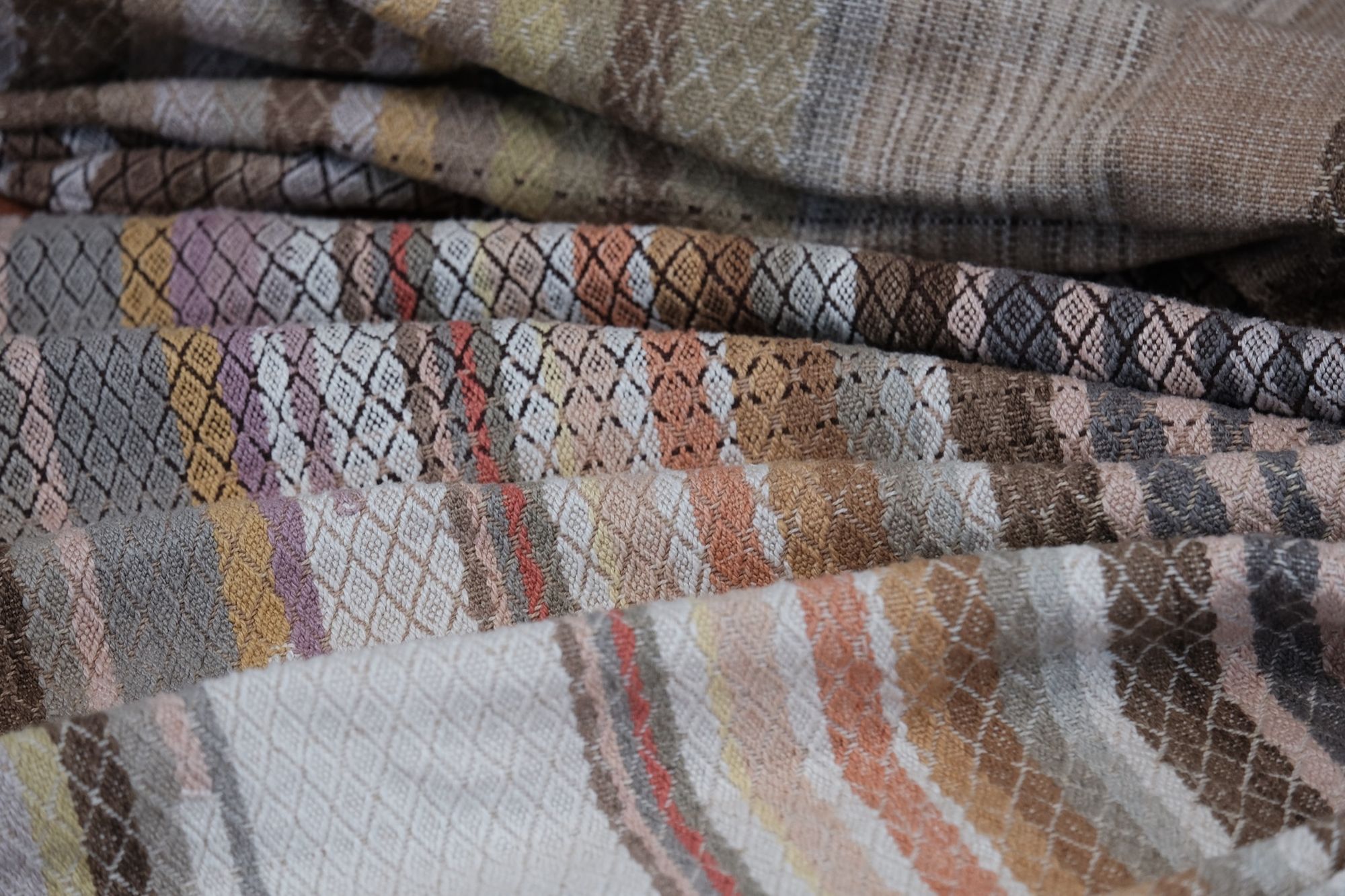 handwoven fabric of Naturally dyed subtle rainbow hues with a diamond texture pattern lays on a wooden floor