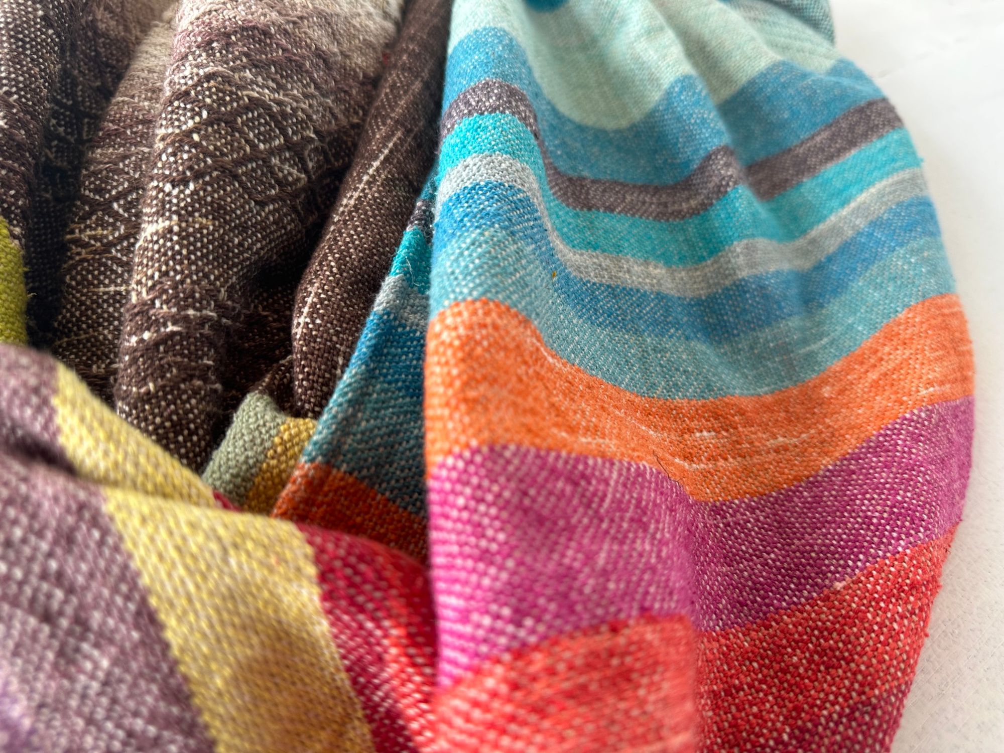 A detail of raw silk handwoven fabric in a rainbow of hand dyed colors with circular moon-like details 