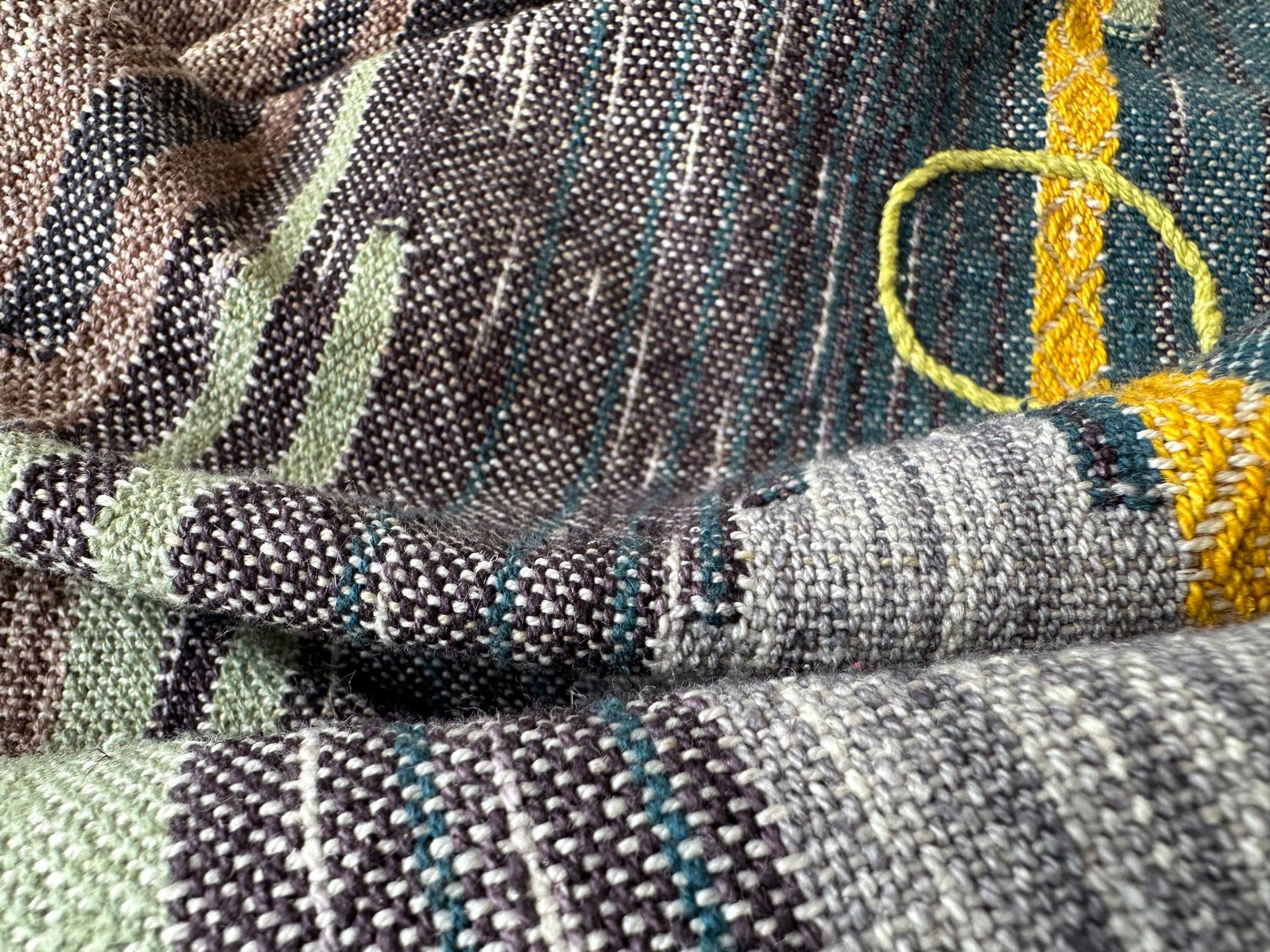 A detail of raw silk handwoven fabric in a rainbow of hand dyed colors with circular moon-like details 