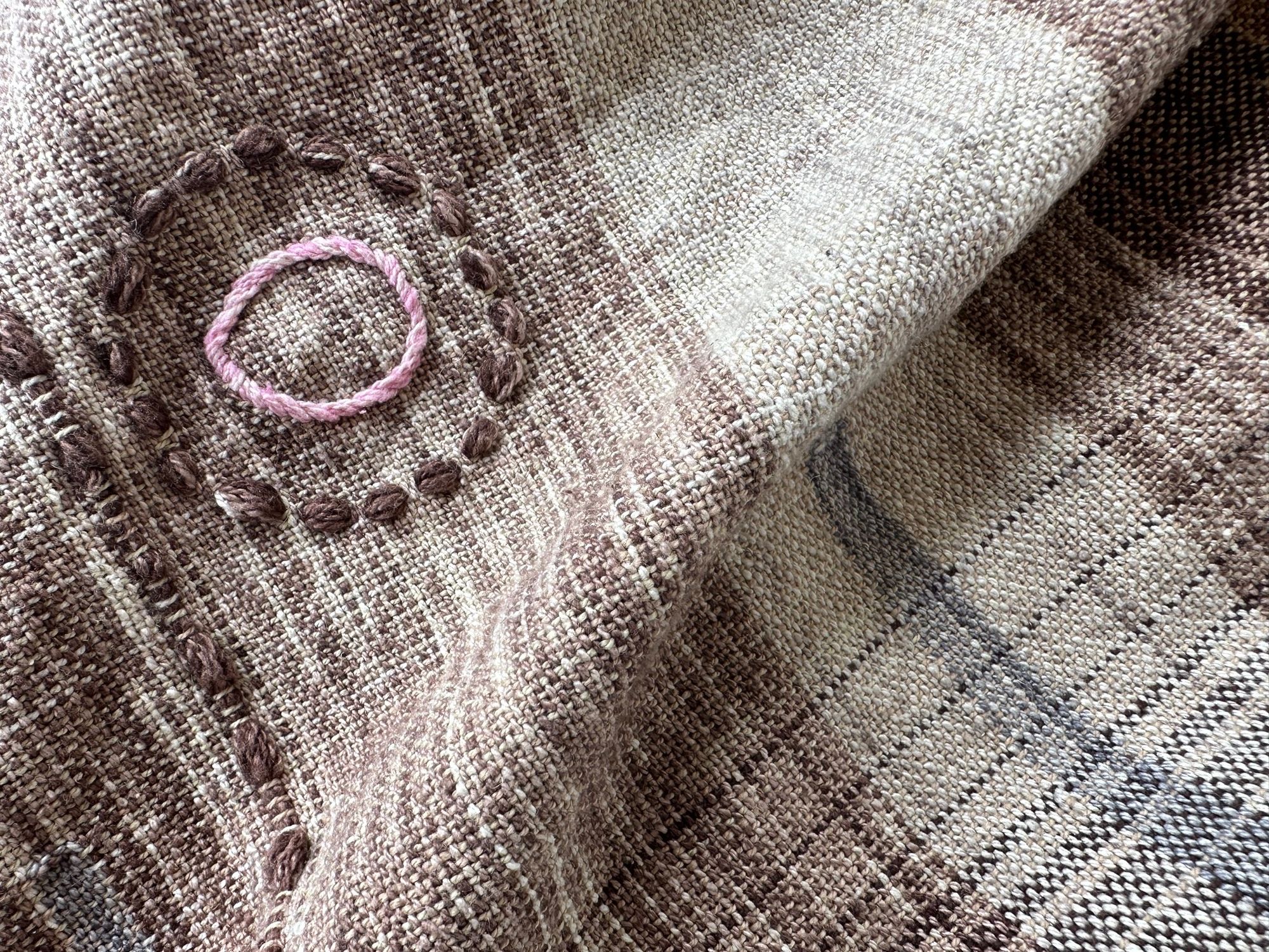 A detail of raw silk handwoven fabric in a rainbow of hand dyed colors with circular moon-like details 