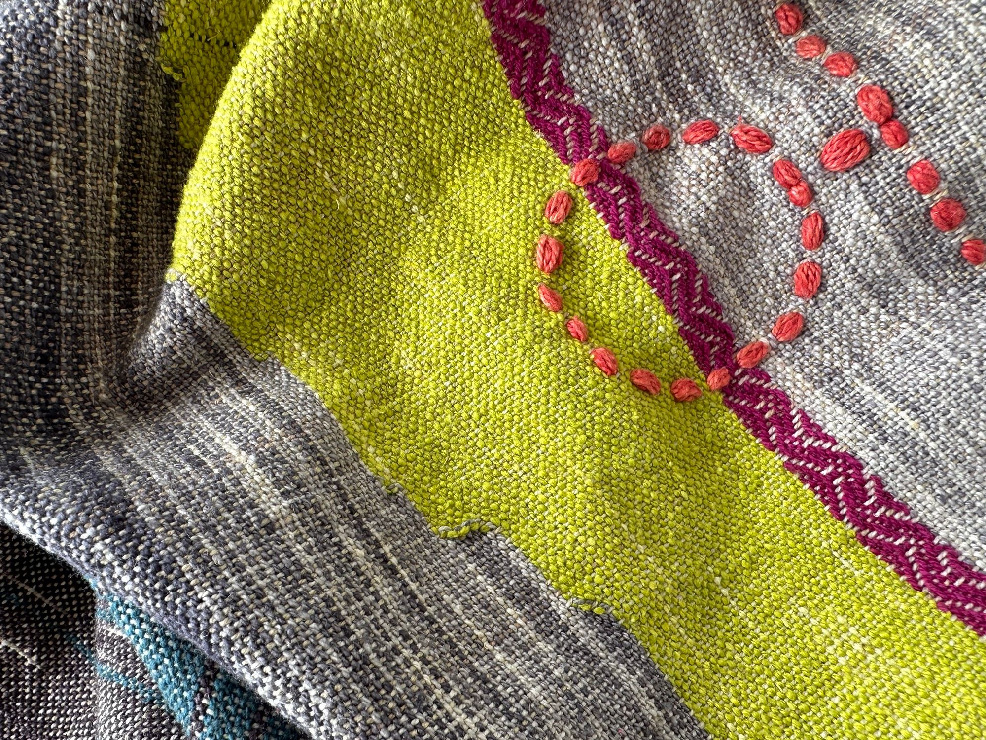 A detail of raw silk handwoven fabric in a rainbow of hand dyed colors with circular moon-like details 