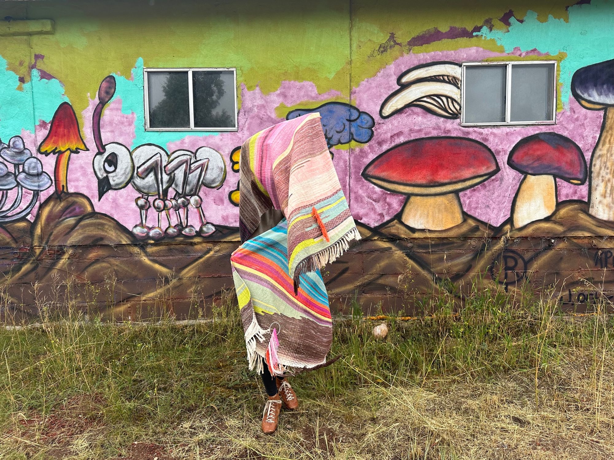 A woman wearing a raw silk handwoven fabric in a rainbow of hand dyed colors with circular moon-like details against a mural of mushrooms