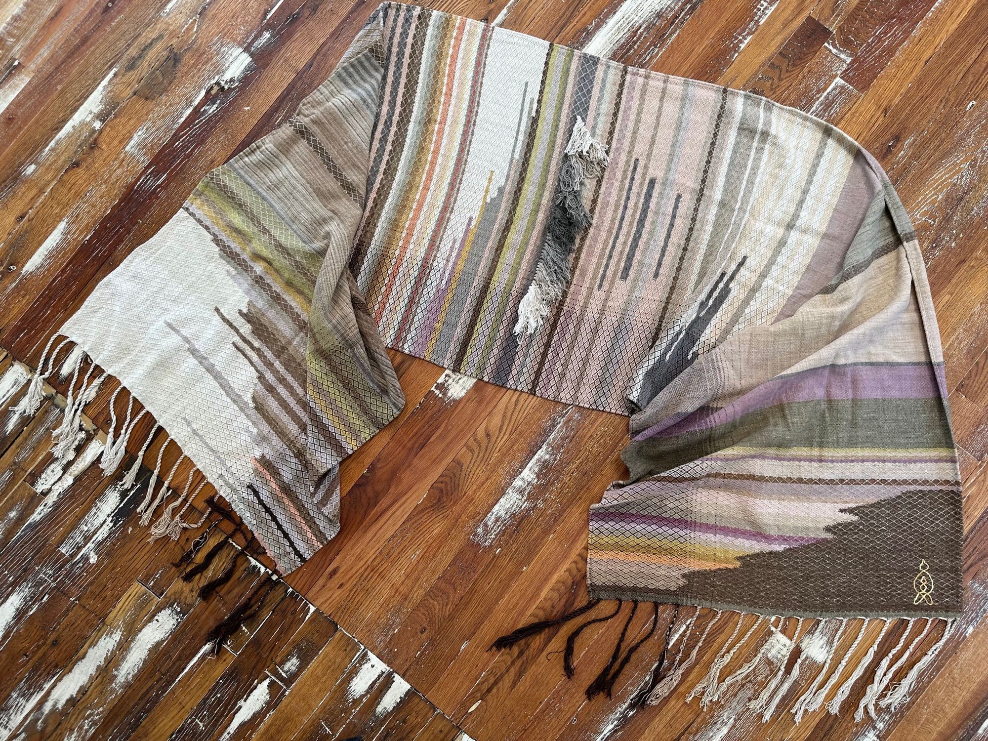 handwoven fabric of Naturally dyed subtle rainbow hues with a diamond texture pattern lays on a wooden floor