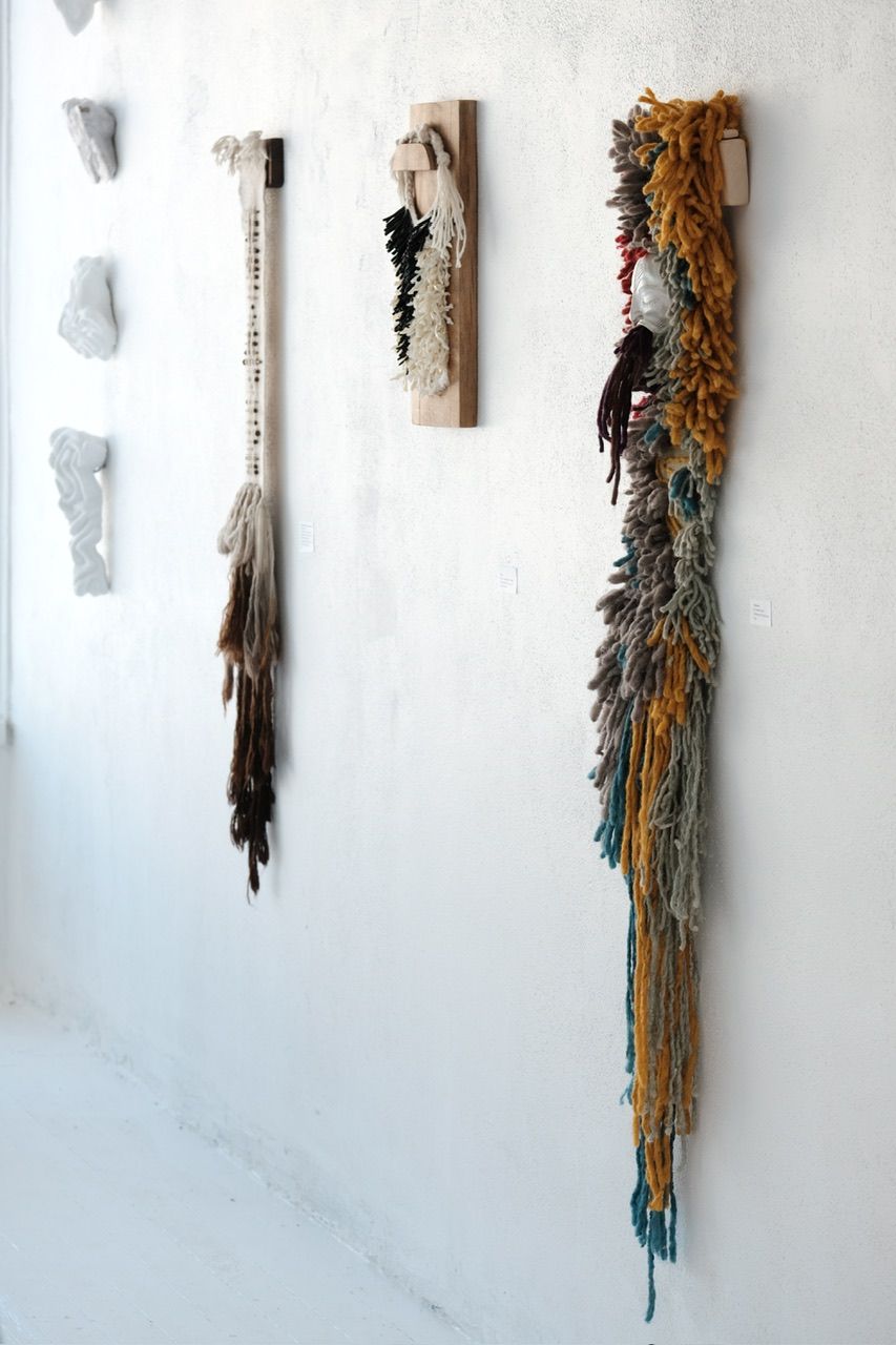 A handwoven sculptural necklace of black coral and mother of pearl hanging on a wooden frame On a white wall