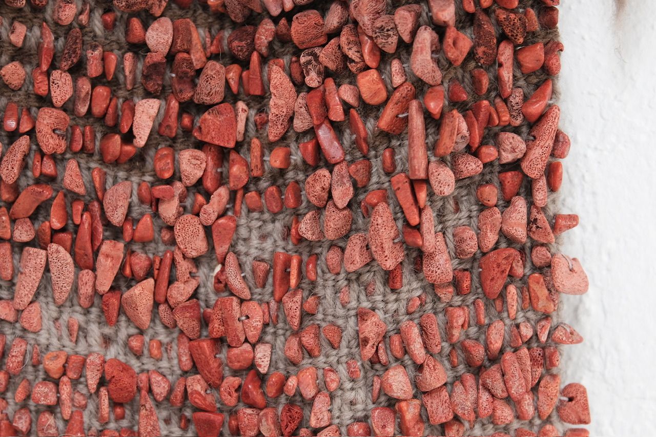 A detail of Red Coral & Wool Adornment hanging on a small oak frame on a white wall