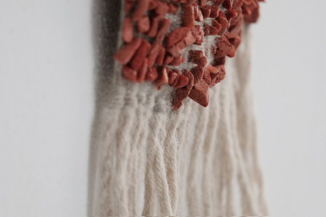 A detail of Red Coral & Wool Adornment hanging on a small oak frame on a white wall