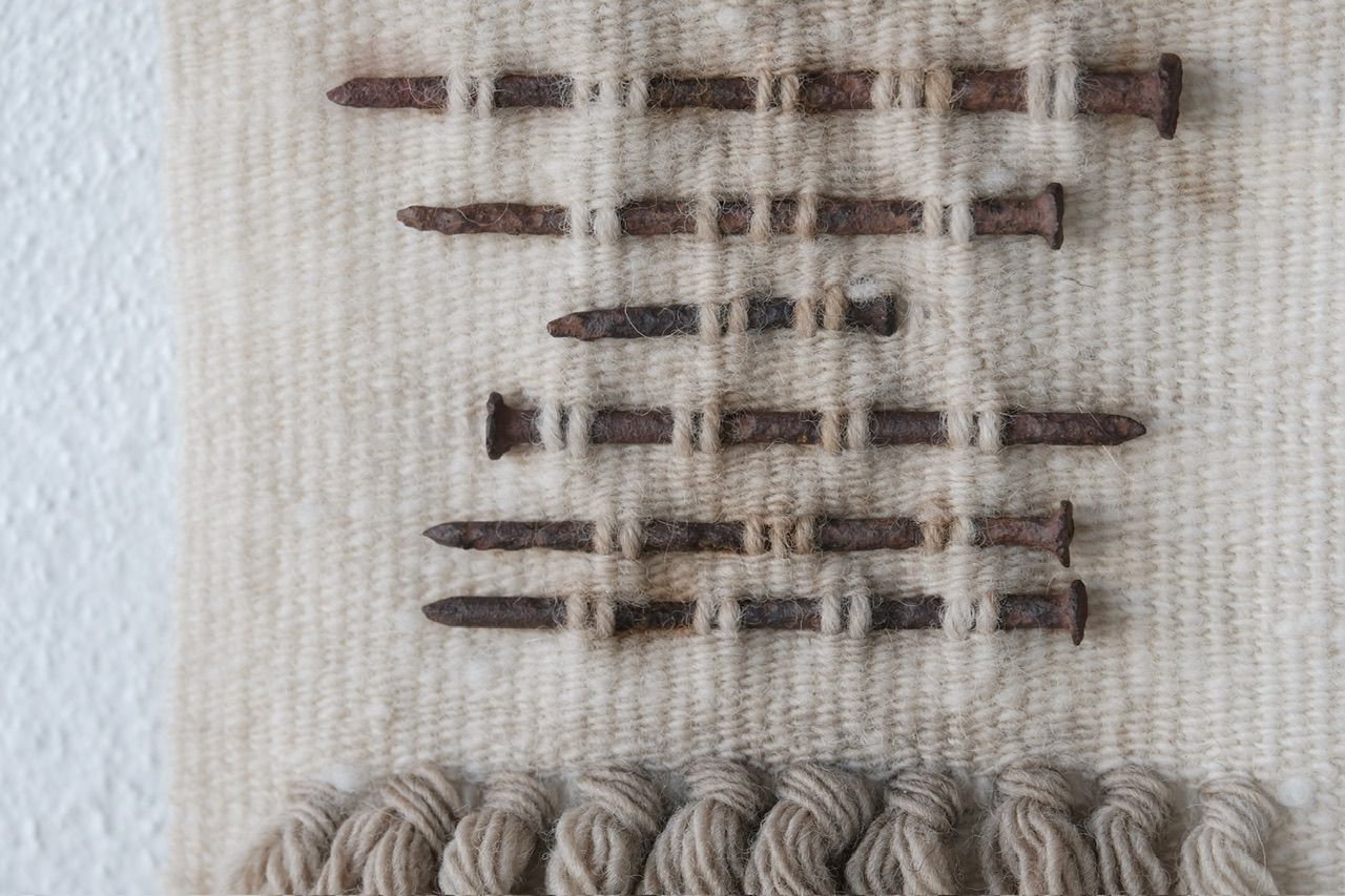 Handwoven wool, walnut wood and rusty nails wall hanging sculpture with long brown shaded fringe on a white wall