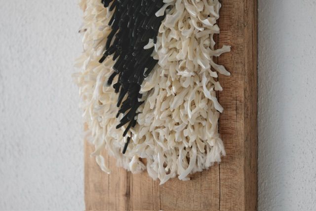 A handwoven sculptural necklace of black coral and mother of pearl hanging on a wooden frame On a white wall