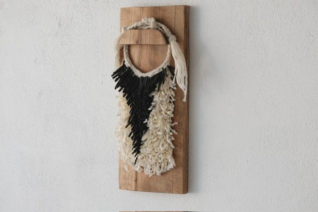 A handwoven sculptural necklace of black coral and mother of pearl hanging on a wooden frame On a white wall