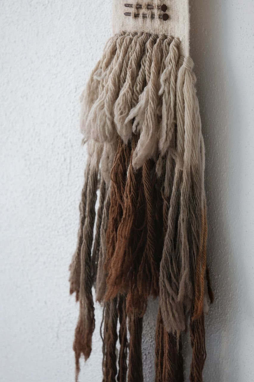 Handwoven wool, walnut wood and rusty nails wall hanging sculpture with long brown shaded fringe on a white wall