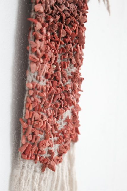 A detail of Red Coral & Wool Adornment hanging on a small oak frame on a white wall