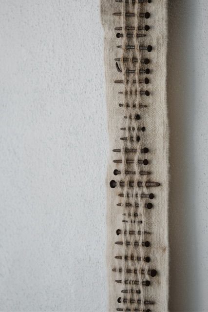 Handwoven wool, walnut wood and rusty nails wall hanging sculpture with long brown shaded fringe on a white wall