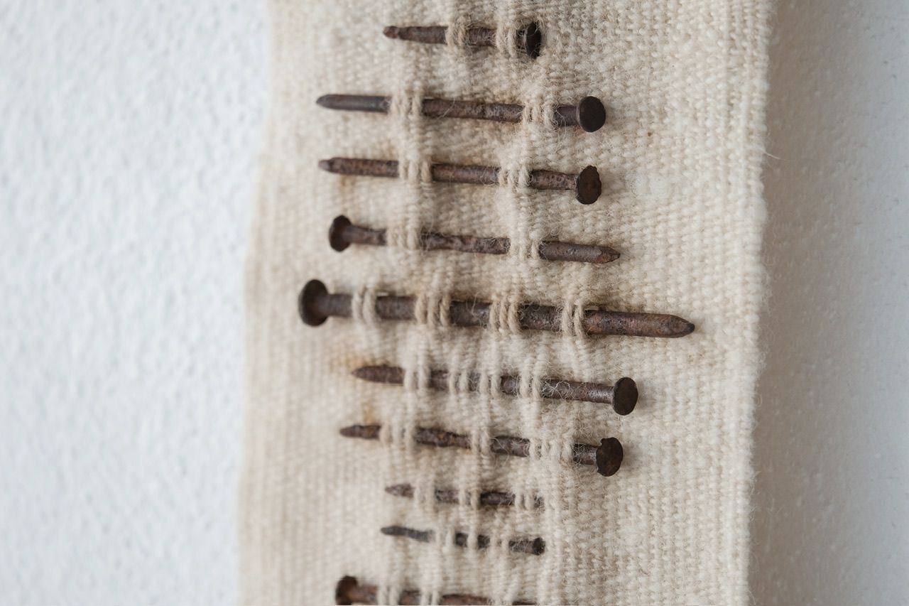 Handwoven wool, walnut wood and rusty nails wall hanging sculpture with long brown shaded fringe on a white wall